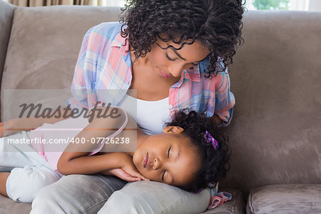 Cute daughter sleeping across mothers lap on the sofa at home in the living room