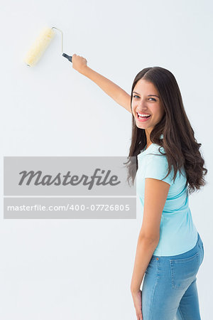 Happy young brunette painting with roller on white background