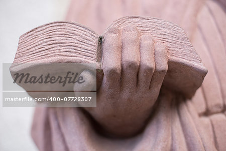 A hand holding a book, statue of stone