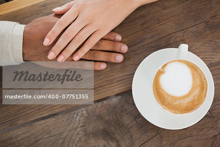 Couple holding hands beside cappuccino at the coffee shop