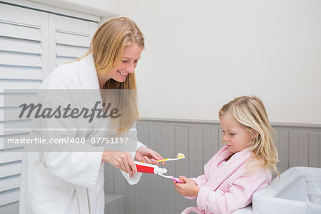 Happy mother and daughter brushing their teeth at home in the bathroom