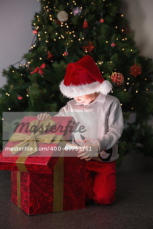 Child opening his christmas present with tree behind him