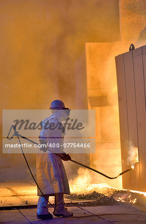 A steel worker takes a sample of hot steel