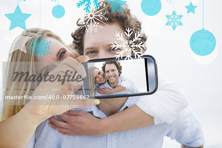 Hand holding smartphone showing man piggybacking woman at beach