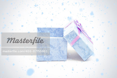 Snow falling against blue gift box with purple ribbon leaning against another