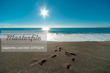 Sunny day, blue sea and footprints in the sand