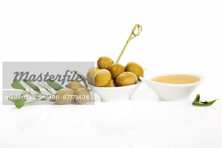 Delicious green olives and extra virgin olive oil in white round bowls with olive tree twig and leaves isolated on white background. Culinary eating.