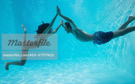 Side view of couple holding hands and swimming underwater in the swimming pool