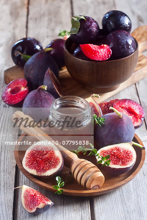 Ripe purple figs, plums, thyme and homey on olive board. Selective focus.