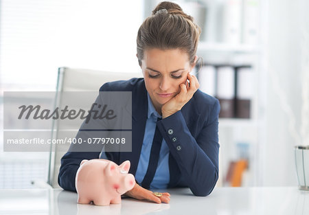 Portrait of sad business woman with piggy bank looking on coin