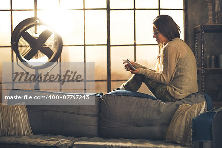 Young woman sitting in loft apartment and using tablet pc