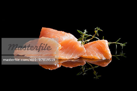 Smoked salmon pieces isolated on black background with fresh herbs. Culinary seafood.