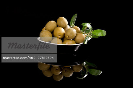 Delicious green olives in black bowl isolated on black background. Luxurious culinary starter.