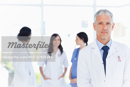 Mature doctor standing in the foreground wearing  breast cancer awareness ribbon