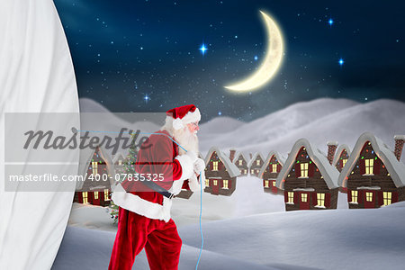 Santa claus pulling rope against cute christmas village at night