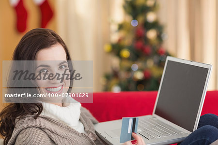 Brunette shopping online with laptop at christmas at home in the living room
