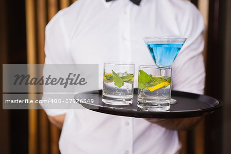 Cheerful young waiter holding tray with cocktails in a bar