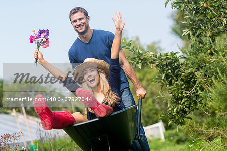 Man pushing his girlfriend in a wheelbarrow at home in the garden