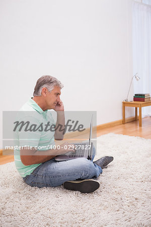 Mature man sitting on rug using laptop at home in the living room