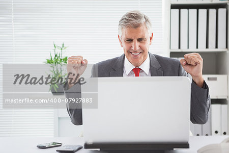 Cheering businessman at his desk in his office