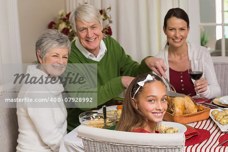 Smiling grandfather carving chicken during christmas dinner at home in the living room