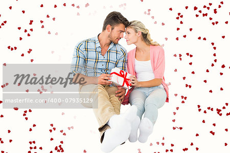 Attractive young couple sitting holding a gift against red love hearts