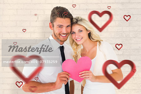 Attractive young couple holding pink heart against white wall