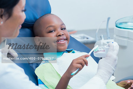 Dentist teaching happy boy how to brush teeth in the dentists chair