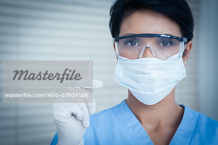 Portrait of female dentist in surgical mask holding dental tool