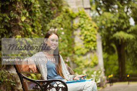 Smiling student sitting on bench holding her mobile phone in park at school
