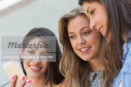 Happy students looking at smartphone outside on campus at the university