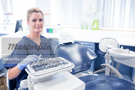 Dentist sitting with tray of tools smiling at camera at the dental clinic