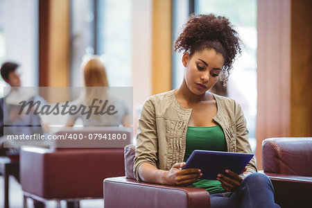 Focused student sitting on sofa using her tablet pc at the univeristy