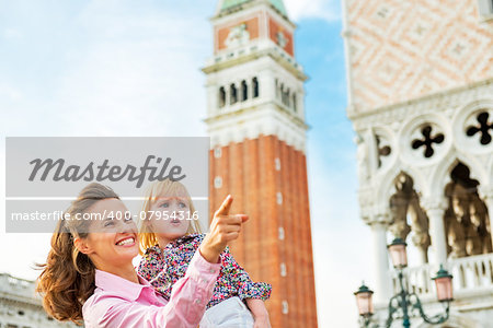 Happy mother pointing baby on something while standing against campanile di san marco in venice, italy