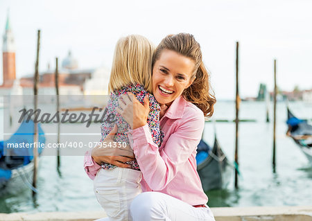 Portrait of happy mother and baby hugging on grand canal embankment in venice, italy