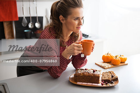 Happy young housewife drinking tea with freshly baked pumpkin bread with seeds in kitchen