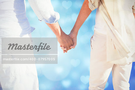 Couple on the beach looking out to sea holding hands against valentines heart design