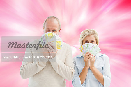 Happy mature couple smiling at camera showing money against digitally generated girly heart design