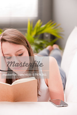 girl reading and studying while lying on her sofa in her living room