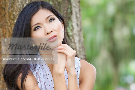 Outdoor portrait of a beautiful young Chinese Asian young woman or girl with natural green background