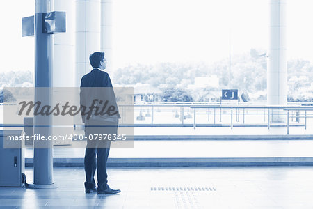 Rear view full body Asian Indian business man waiting bus at public bus station, in blue tone.