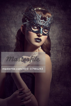 Gorgeous, mysterious female in carnival, silver mask, with brown long hair and dark make up wearing black dress.