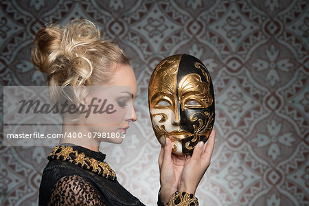 blonde sensual woman with antique gothic carnival dress and baroque jewellery posing with theatrical mask in the hands
