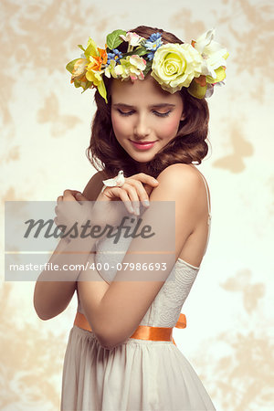 Attractive, brunette spring woman in white dress. She has got little bird on her finger and wreath of flowers on her head.