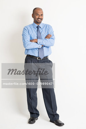 Full body Indian businessman arms crossed standing on plain background with shadow
