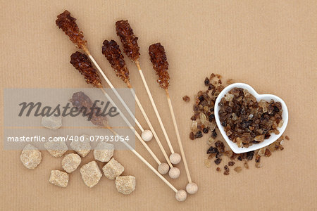 Brown sugar cubes, lollipops and crystal chunks over brown paper background.