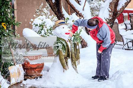 A woman is making a snowman in her front yard during snow storm
