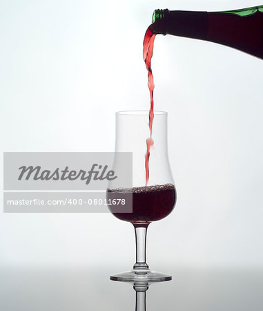 Pouring red wine in a glass on white background