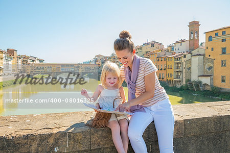 Mother and baby girl sitting on bridge overlooking ponte vecchio in florence, italy and looking at map