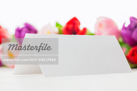 Close up of colorful tulips and white card on wooden table